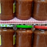 Jar of homemade apple jam with fresh apples and spreader