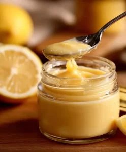 Bowl of homemade Instant Lemon Curd with fresh lemons and a whisk