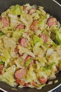 Cabbage with peppers, onion, sausage, and bacon in a skillet