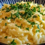 A bowl of steaming noodles garnished with fresh vegetables and herbs.