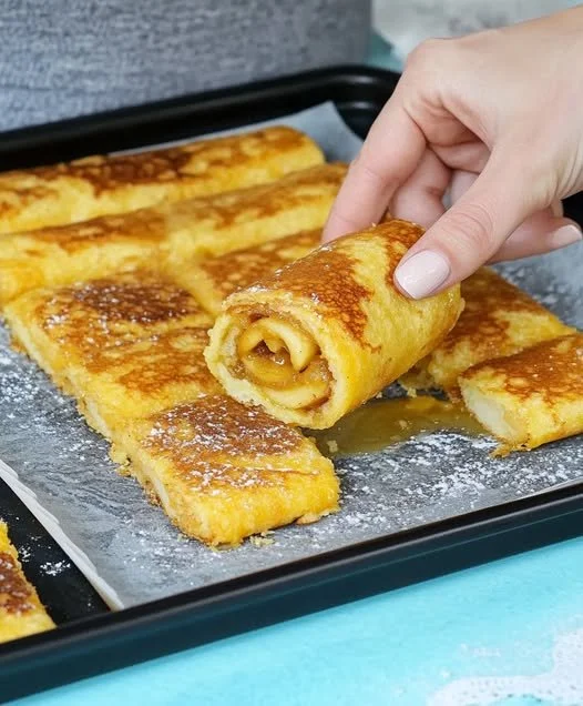 Oven-baked apple pancake roll topped with powdered sugar and served on a plate