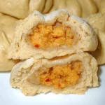 Freshly steamed bun filled with savory ingredients on a wooden table.