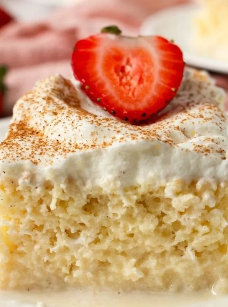 A slice of Three Milks Cake topped with whipped cream and berries, showcasing its creamy texture.